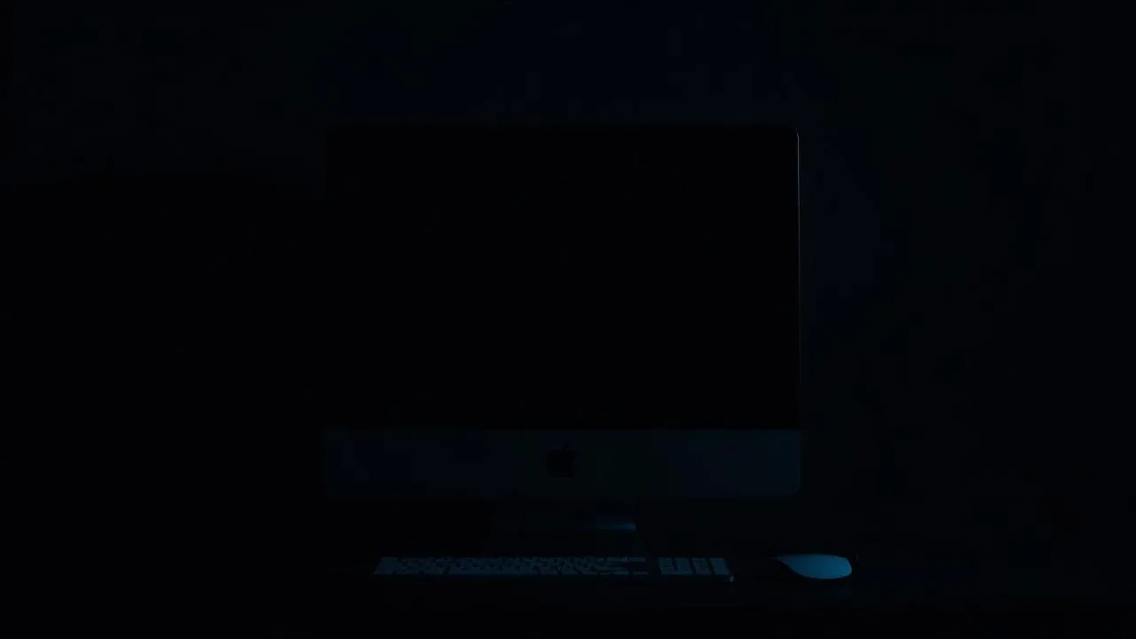 Old silver Intel iMac with screen off on a dark desk under cool blue light